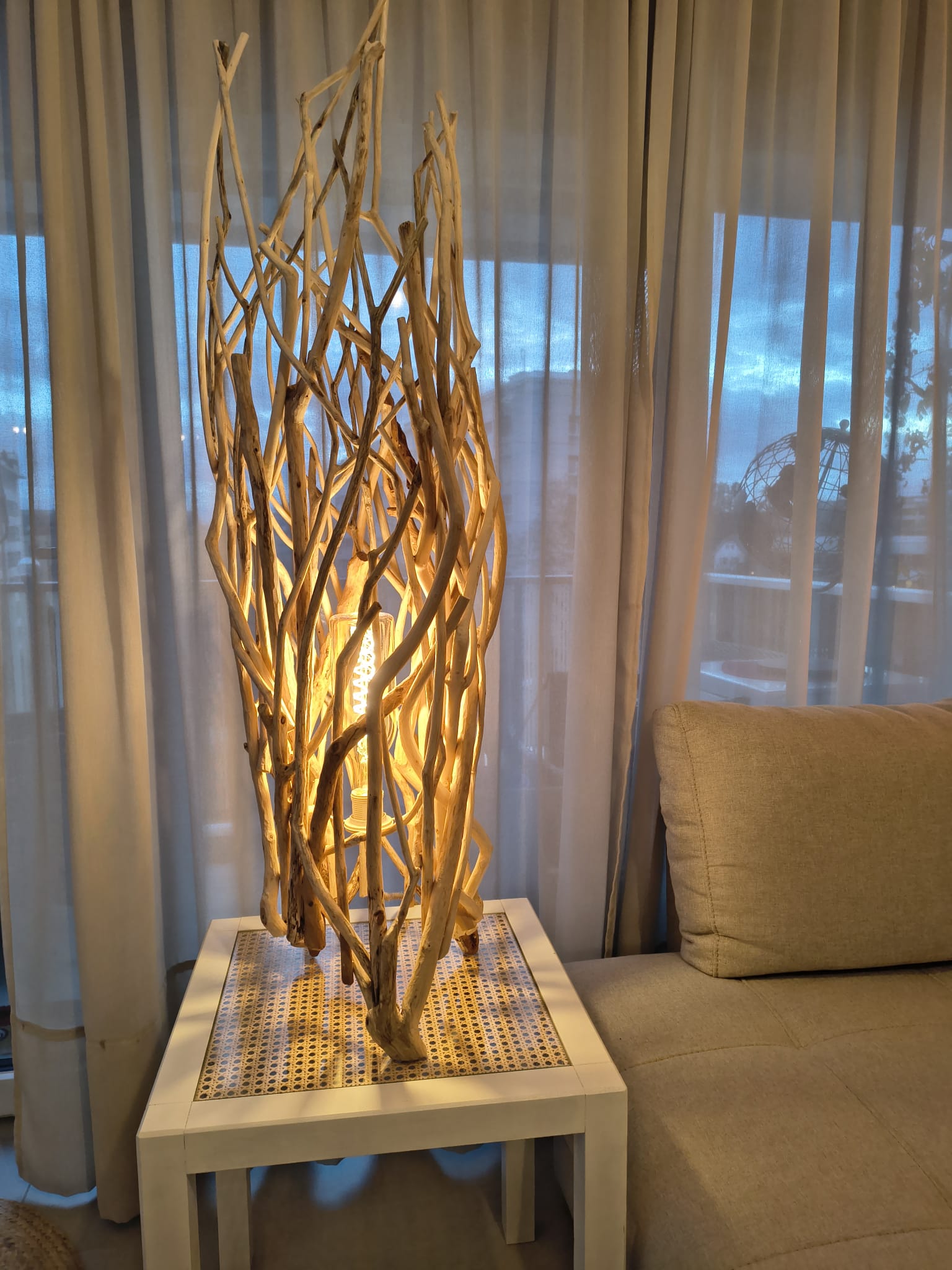 Lampe conique haute faite de bâtons de bois flotté noués en fuseau, posée sur une table d'appoint